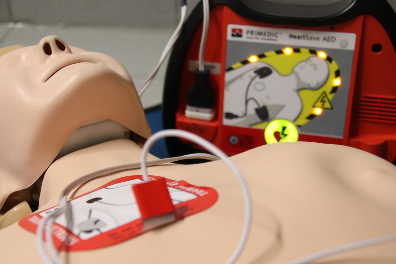 CPR dummy with AED pads attached, next to an automated external defibrillator in use.