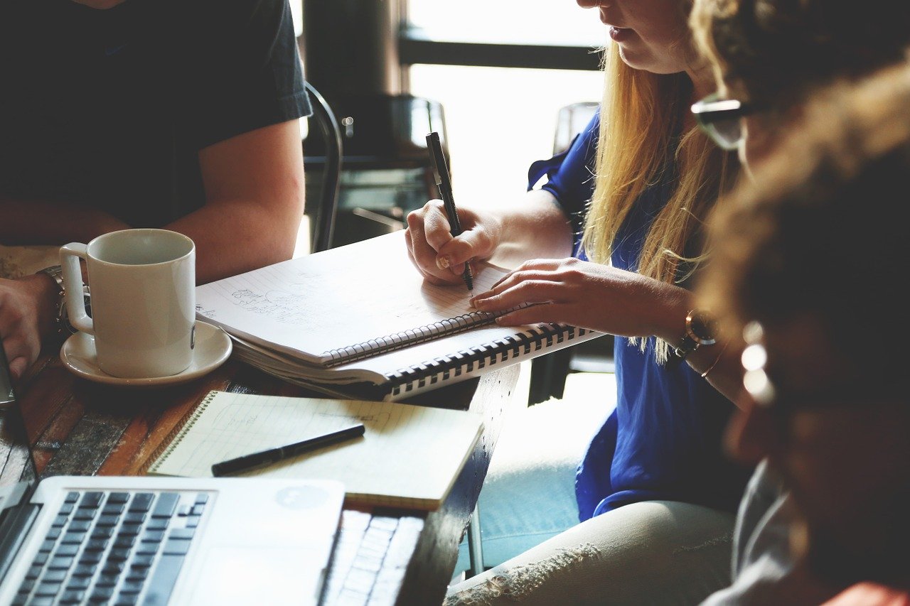 People working together at a table with notebooks, coffee, and a laptop.