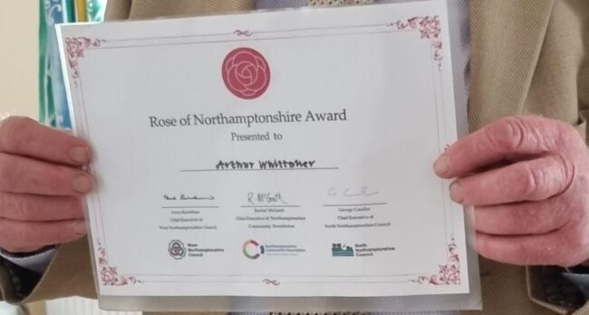 A Whittaker Rose of Northamtonshire Award 23 A Whittaker Rose of Northamtonshire Award 23, A person holds a Rose of Northamptonshire Award certificate with signatures and logos.