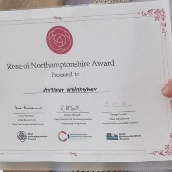 A Whittaker Rose of Northamtonshire Award 23 A Whittaker Rose of Northamtonshire Award 23, A person holds a Rose of Northamptonshire Award certificate with signatures and logos.